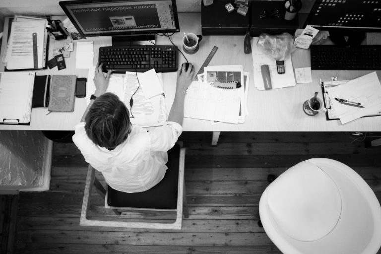 Le corps, grand oublié de la performance au travail Black and white image of an employee working at a desk with papers and computer.
